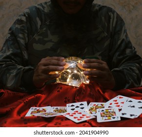 A fortune teller man is predicting the future with a crystal ball on a table with cards.