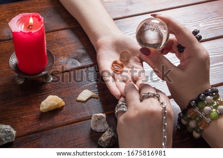 A fortune teller predicts the fate of love with wedding rings, a magic ball, lighted candles and magic stones. A Gypsy woman performs a love spell. A clairvoyant palmist reads by hand with a candle.