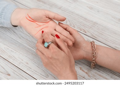 Fortune teller reading lines on woman's palm at white wooden table, closeup. Chiromancy