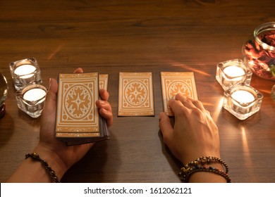 Fortune teller reading tarot cards concept.Tarot reader hands holding facing down tarot cards and picking.The burning candles on a wooden table.Mystic and darkness background. - Shutterstock ID 1612062121