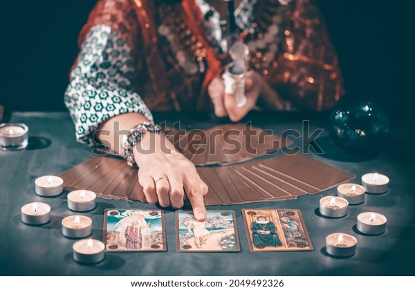 Fortune teller with tarot cards on table near\
burning candles.Tarot cards spread on table with crystal\
ball.Forecasting\
concept.