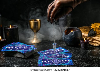 Fortune teller using pendulum and tarot cards to read future on dark background