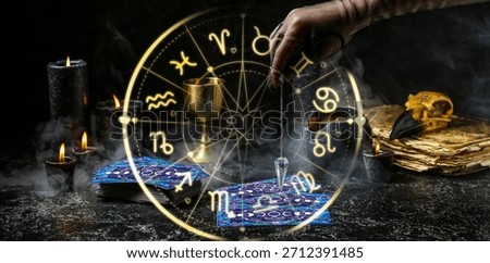 Fortune teller using pendulum and tarot cards for future reading on dark background, closeup