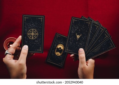Fortune teller woman and a black tarot cards over red table background and candles.