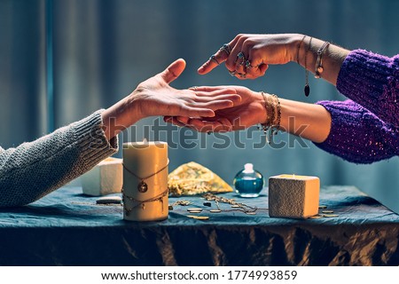 Fortune teller woman reading palm lines around candles and other magical accessories. Witch during fortune telling, palmistry and divination. Magic ritual 
