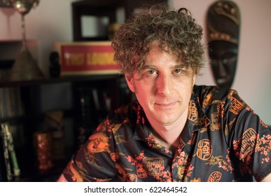 Forty Something Single  Man Posing In Bachelor Pad. Long, Curly, Brunette Hair. Tiki Decor.