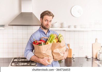 Forty Years Old Caucasian Man Holding Paper Grocery Shopping Bags In The Kitchen. 