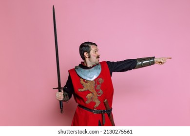 Forward to attack. Comic portrait of medieval warrior or knight wearing wearing armor clothing holding big sword isolated over pink background. Comparison of eras, history, funny meme emotions