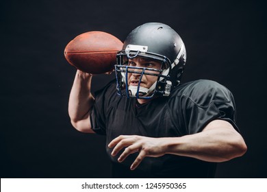 Forward Man In Black Protective Uniform Throwing A Ball In A Professional American Football Game, Isolated Studio Shot Over White Background. Sport Concept