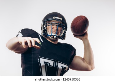 Forward Man In Black Protective Uniform Throwing A Ball In A Professional American Football Game, Isolated Studio Shot Over White Background. Sport Concept