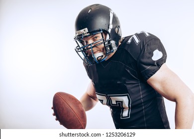 Forward Man In Black Protective Uniform Throwing A Ball In A Professional American Football Game, Isolated Studio Shot Over White Background. Sport Concept