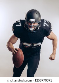 Forward Man In Black Protective Uniform Throwing A Ball In A Professional American Football Game, Isolated Studio Shot Over White Background. Sport Concept