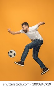 Forward To The Victory.The Young Man As Soccer Football Player Jumping And Kicking The Ball At Studio On A Yellow Background. Football Fan And World Championship Concept. Human Emotions Concepts