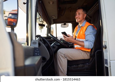 Forwarder or truck driver in drivers cap holding mobile phone