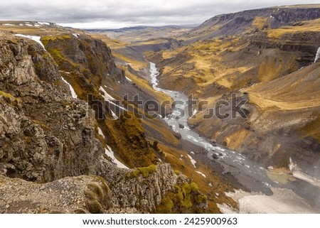 Fossardalur valley landscape with vertical cliffs covered with grass and moss, glacial Fossa river flowing below, view from Haifoss waterfall, Iceland.