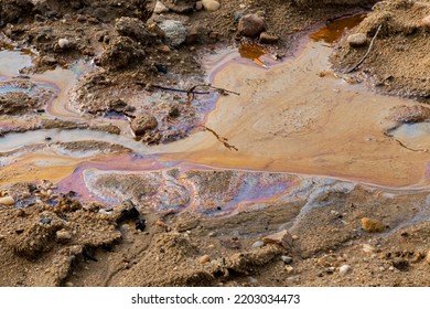 Fossil Fuel Pollution In The Water And On The Sand. Oil Spill In The Environment And A Cigarette Butt. Spectral Colors Of Light Are Visible. The Nature Is Contaminated By A Leak In A Pipe.