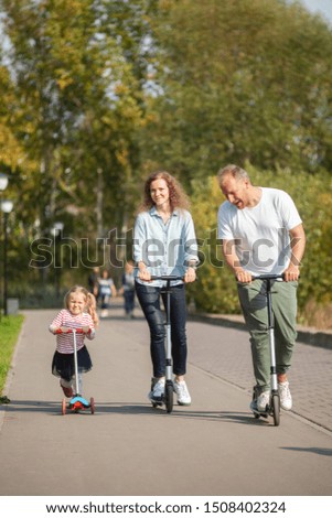 Fother, mother and daughter riding on scooters in a park on sunny summer day