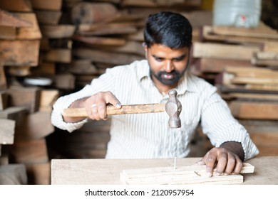 Foucs On Hammer, Young Indian Carpenter Busy Hitting Nails Using Hammer To Wood At Shop - Concept Of Craftperson, Blue Collar Job And Skilled Manual Labour.