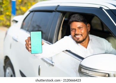 Foucs on mobile, cab driver showing mobile phone with green screen mockup by looking at camera - concept of online booking servive, app advertising for travel service and promotions