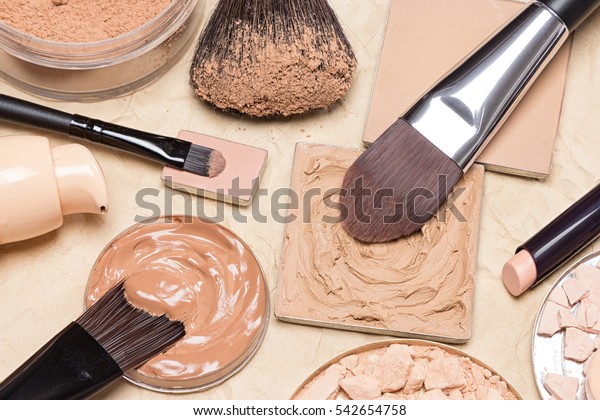 Foundation, powder, concealer pencil with make\
up brushes on crumpled paper. Makeup products to even out skin tone\
and complexion