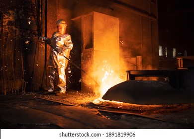 Foundry worker in aluminized protective fire suit checking temperature of molten iron in furnace. Industrial steel production and metallurgy. - Powered by Shutterstock