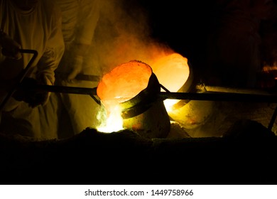 Foundry worker pouring hot molten metal into mold casting - Powered by Shutterstock