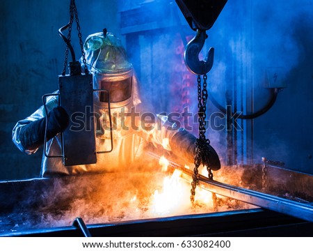 Foundry worker with special protective suit quenching casts in oil bath