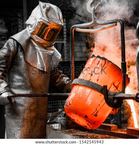 In a foundry workshop. A worker protected by a safety suit pours the molten metal into a mold
