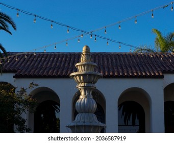 Fountain With Edison Bulb String Lights Crossed Overhead In Front Of Building 