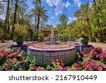 Fountain inside the Palmeral de Elche surrounded by flowers and palm trees. In the municipal park of Elche, Alicante, Spain
