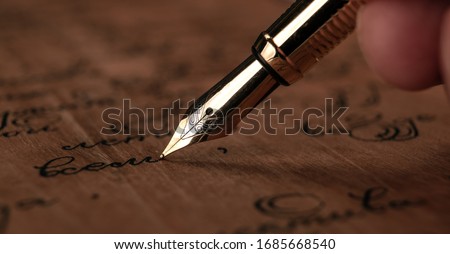 fountain pen in the hand with paper with ink text on the wooden desk closeup
