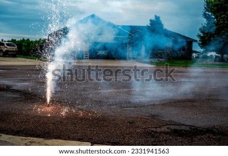 A fountain of sparks, flames, and smoke emitting from a fountain fireworks being set off in a residential neighborhood. 
