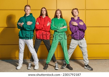 Four active teenagers in modern youth clothes dance street ballet by a bright yellow building and have fun together. Bright youth fashion. Modern teenagers. Street dances.
