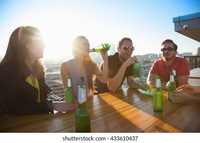 Four Adult Friends Drinking Beer At Rooftop Bar Table With Los Angeles Skyline, USA