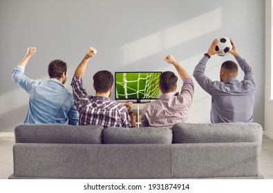 Four adult male friends with arms raised emotionally watching a football match on TV at home. Unrecognizable friends sit on the couch with their backs to the camera and cheer for their favorite team. - Powered by Shutterstock