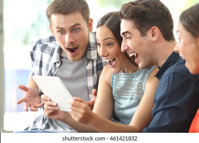 Vier erstaunliche Freunde, die Medieninhalte zusammen in einem Tablett sehen, das auf einem Sofa im Wohnzimmer zu Hause sitzt