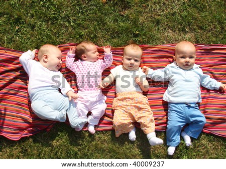 Four babies lying on colourful cloth in park