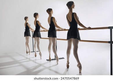 Four ballet dancers, elegant teen girls standing at barre in black costumes and pointe shoes, practicing against grey studio background. Concept of ballet, art, dance studio, classical style, youth - Powered by Shutterstock