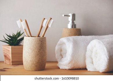 Four bamboo toothbrushes in a cup and white towels