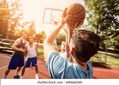 Four Basketball Players Have A Training Outdoor. Selective Focus. Focus On Foreground, On Rear View Man Shooting Free Throw.