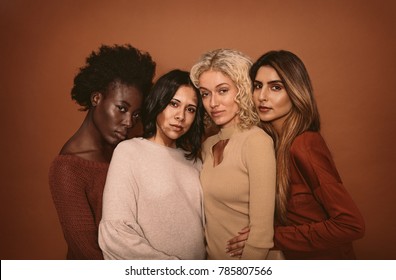 Four Beautiful Girl Friends Standing Together On Brown Background. Multi Ethnic Group Of Women In Studio Looking At Camera.