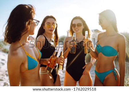 Four beautiful girls cheers and drink beers on the beach, enjoying vacation. Vacation time laughing and smiling.
