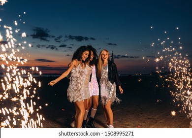 Four beautiful women standing outdoors between fireworks. Happy friends celebrating at sunset. - Powered by Shutterstock