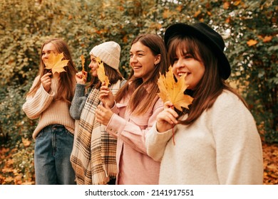 Four best friends company spending time together,gratuated, celebrate, laughing, holding maple leaves near face. Closeup