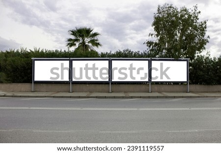Four billboards beside the road and in front of the trees under cloudy blue sky. Mock up billboard for outdoor advertisement. Blank billboards for marketing or any announcement.