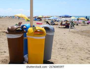 Four Bins For Separate Waste Collection On The Shore Of The Beach Near The Sea And Mountains Umbrella Of Vacationers In Summer