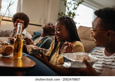 Four Black Friends Used Their Free Time Hanging Together And Just Have Fun. They Are Eating Takeout Food While Sitting On The Floor In The Living Room