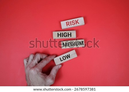 Four blocks labeled low, medium, high, and risk, aligned on an red surface, represent decision making, risk assessment, and organization.