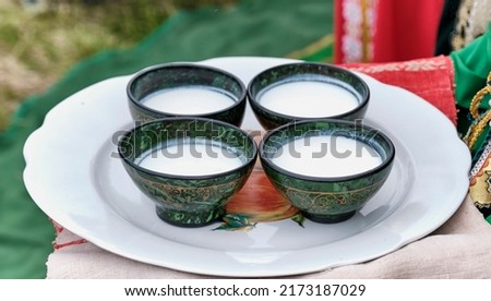 Four bowls with traditional Bashkir pattern, filled with mare's milk or koumiss, national drink, on large flat dish. Folk festival Sabantuy