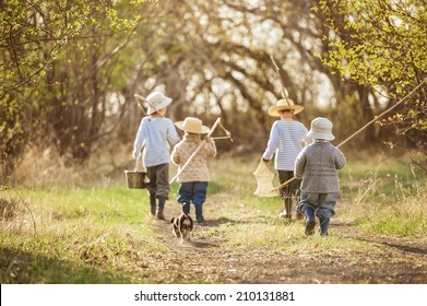 Four Boys With Fishing Rods Go On A Fishing Trip On The Narrow Rural Road In Sunny Summer Day